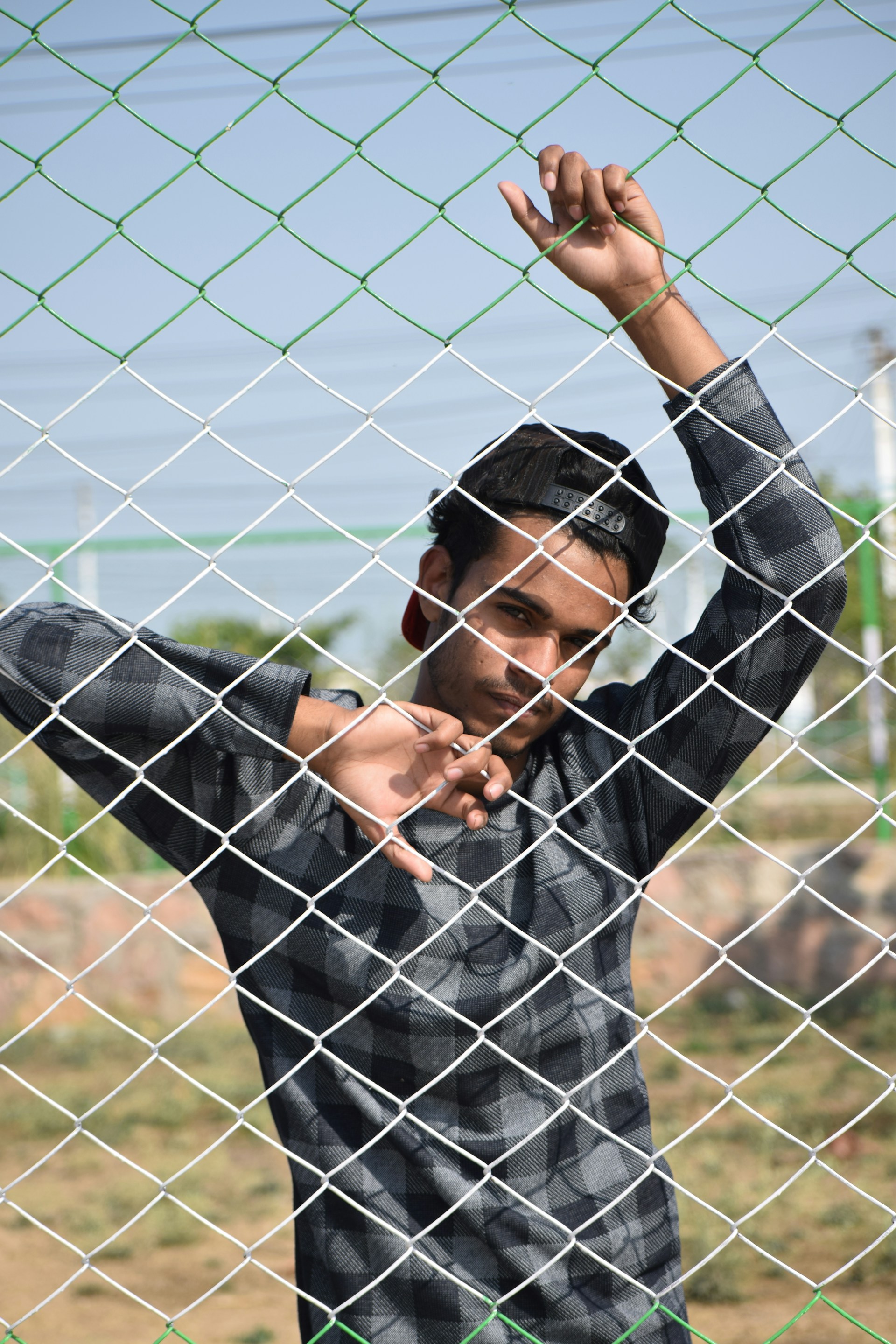 man in black and gray long sleeve shirt holding on gray metal fence during daytime