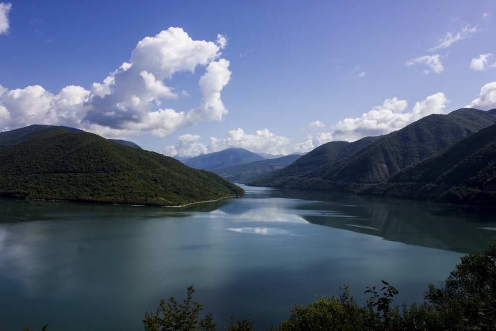 lake in the middle of mountains under blue sky and white clouds during daytime