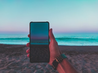 A user scrolling through the Nativo Trancoso app on a smartphone at the beach.
