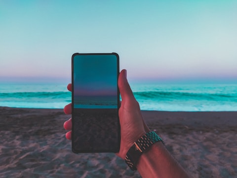 A user scrolling through the Nativo Trancoso app on a smartphone at the beach.