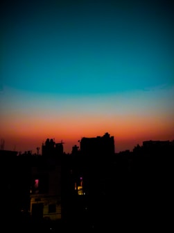 A vibrant sky transitions from deep blue at the top to a warm orange near the horizon. The silhouette of a city skyline is visible with various building outlines against the colorful backdrop, creating a striking contrast.