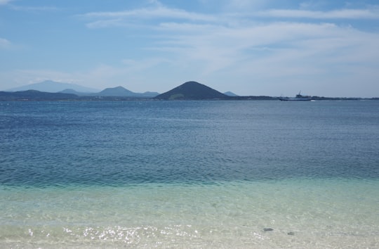 body of water near mountain under blue sky during daytime in Jeju South Korea
