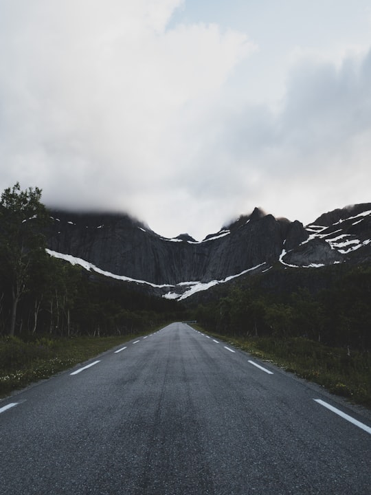 gray concrete road near mountain under white clouds during daytime in Nusfjord Norway