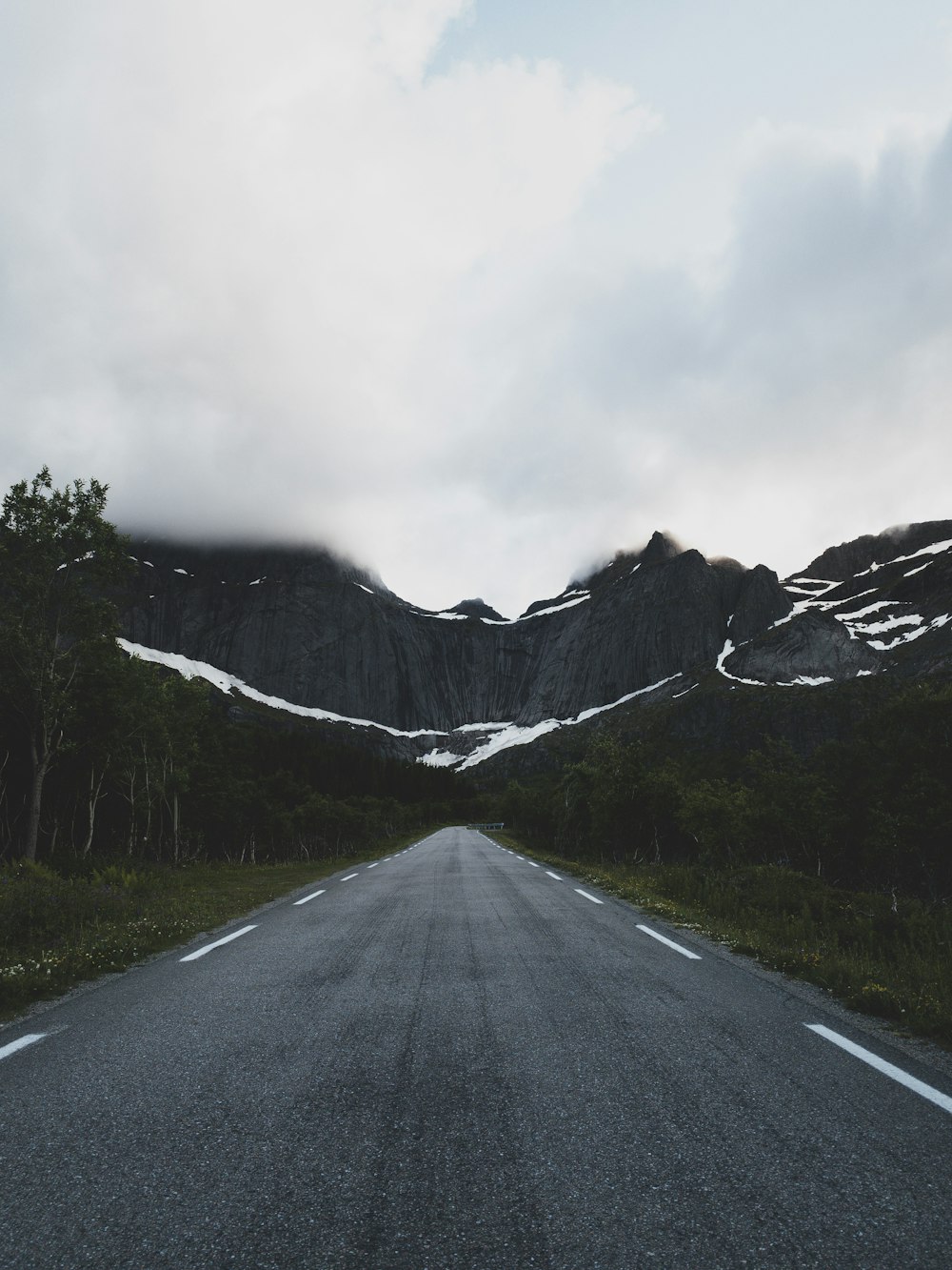 gray concrete road near mountain under white clouds during daytime