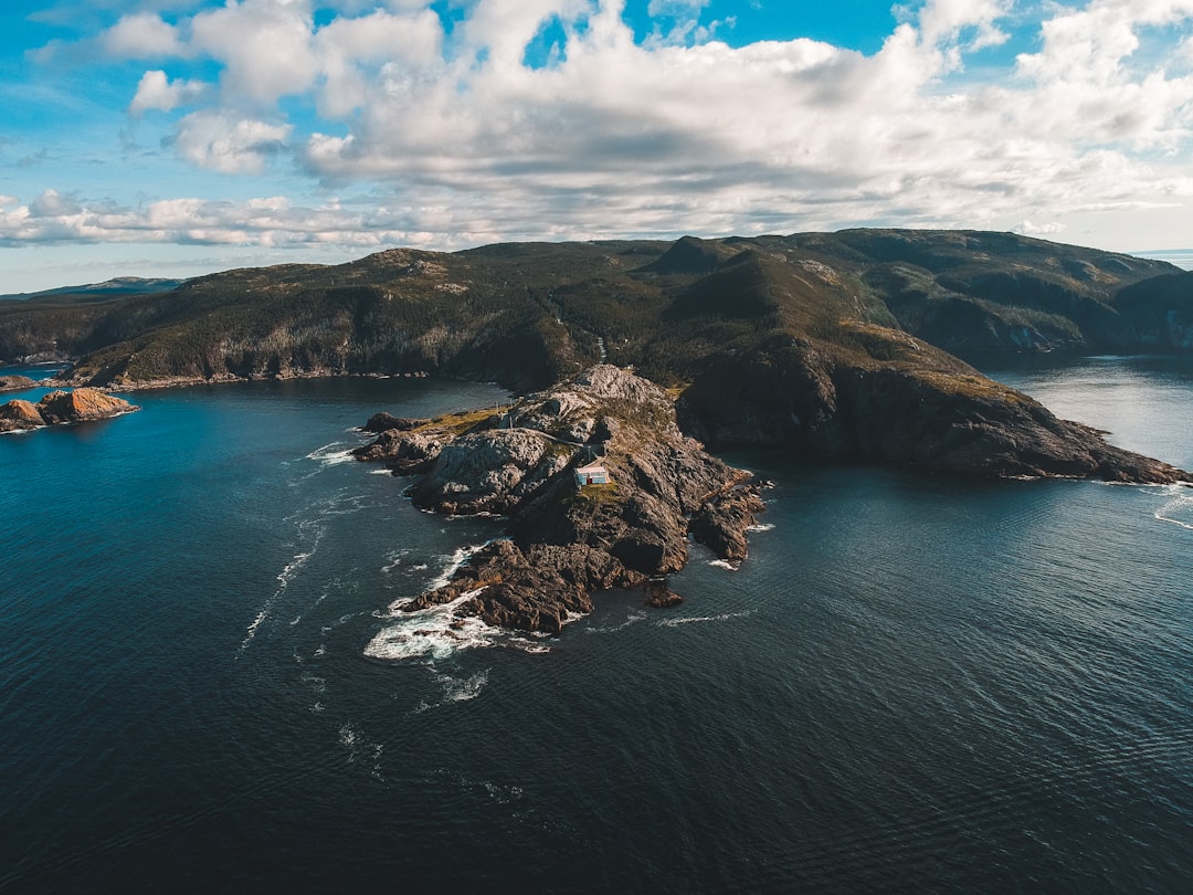 brown and green mountain beside blue sea under blue and white cloudy sky during daytime