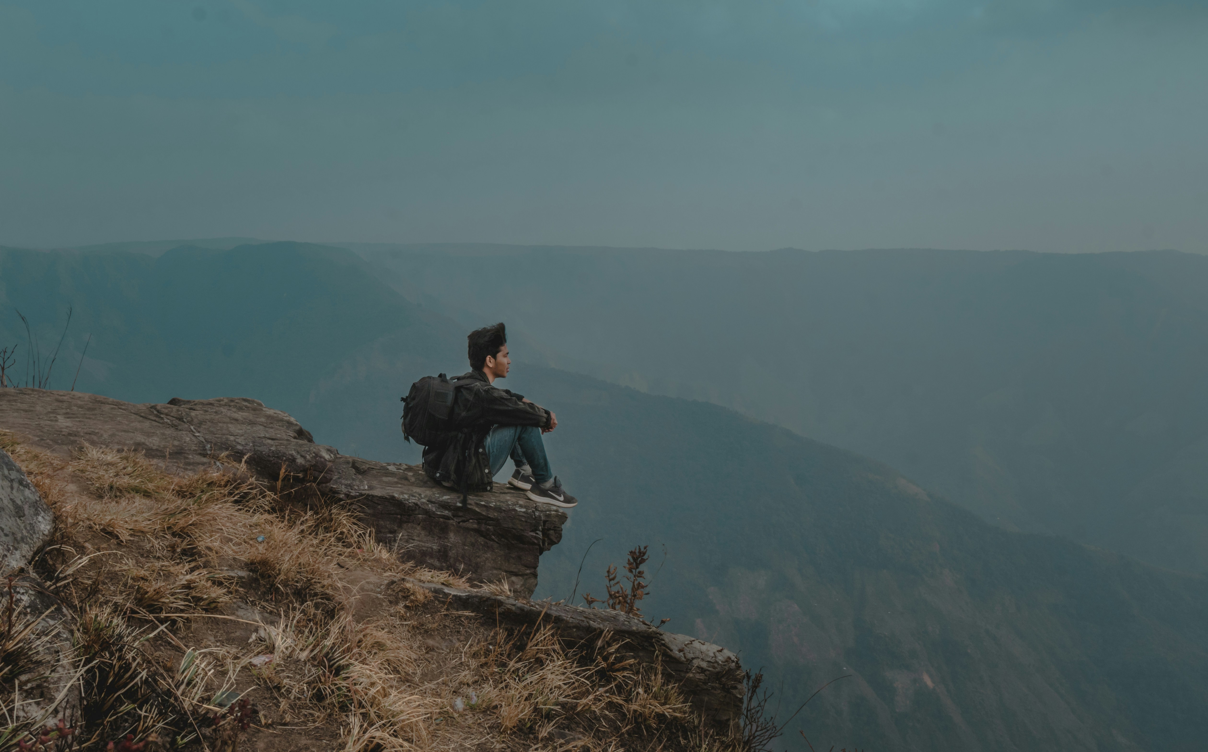 man in black jacket sitting on brown rock formation during daytime