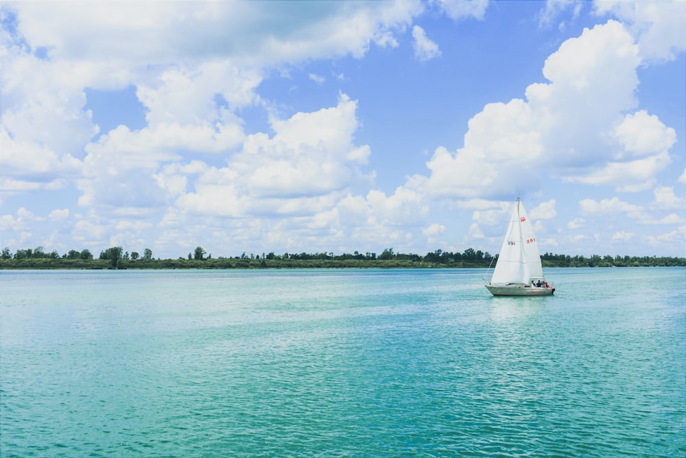 weißes Segelboot auf See unter blauem Himmel und weißen Wolken tagsüber