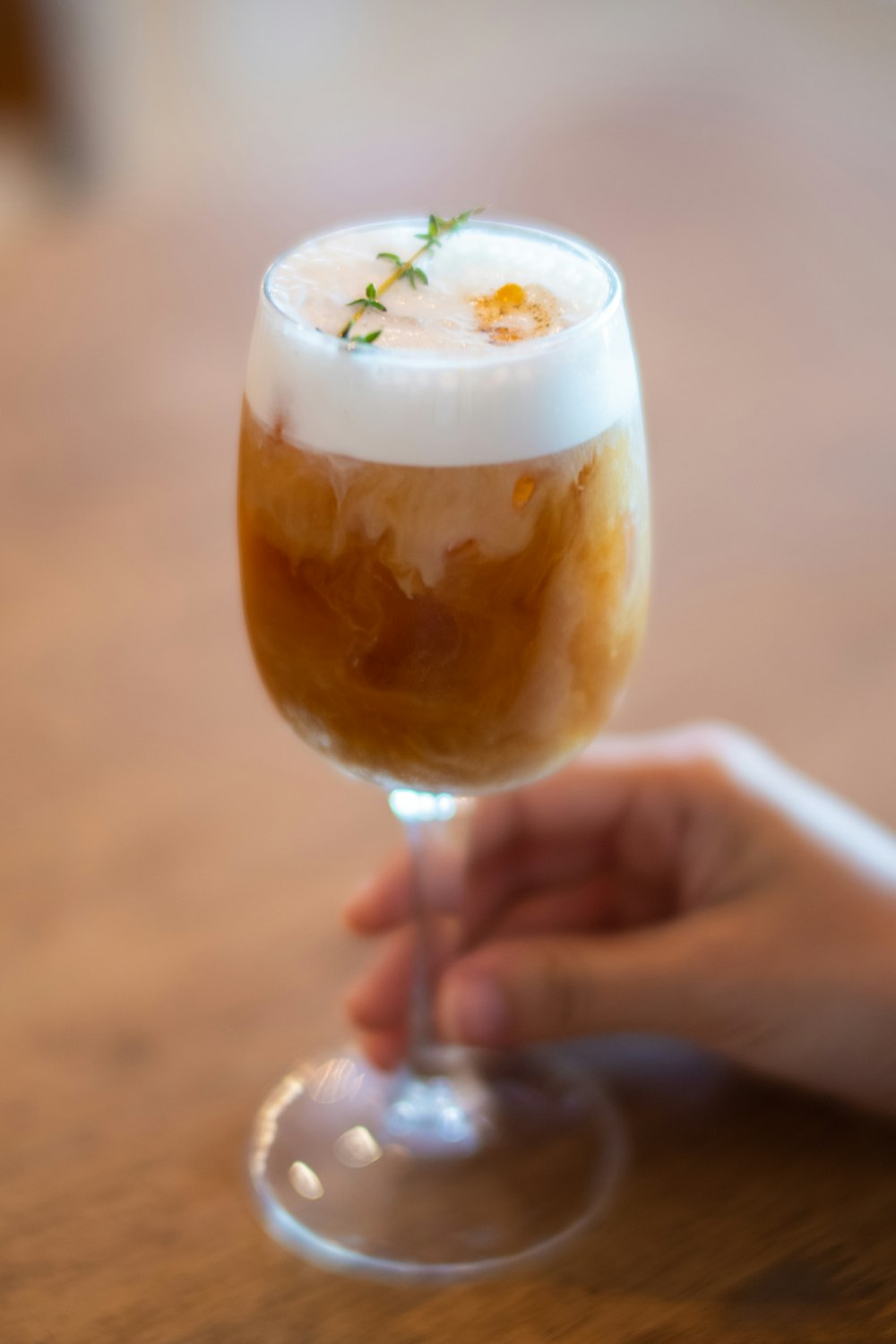 person holding clear footed glass with brown liquid