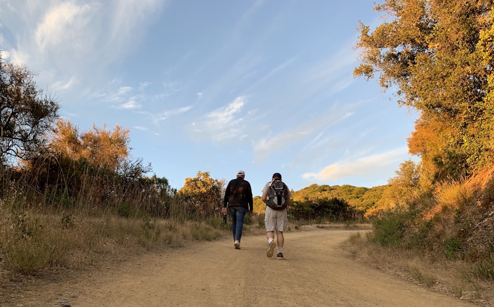 man and woman walking on dirt road between green grass field during daytime