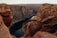 A breathtaking canyon landscape with steep, rugged cliffs surrounding a winding river that carves through the deep valley. The geological formations are composed of rich red and orange hues, emphasizing the dramatic erosion patterns on the rock surfaces.