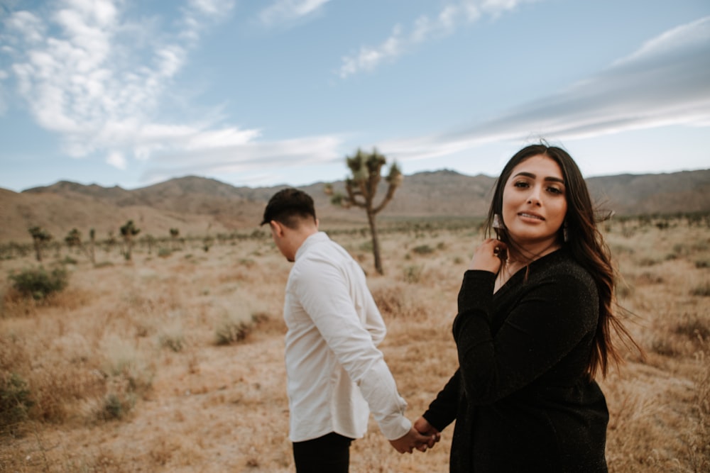 man and woman holding hands while walking on brown field during daytime