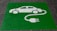A green painted square on a pavement contains a white stencil of a car with a cable and plug, symbolizing an electric vehicle charging station.