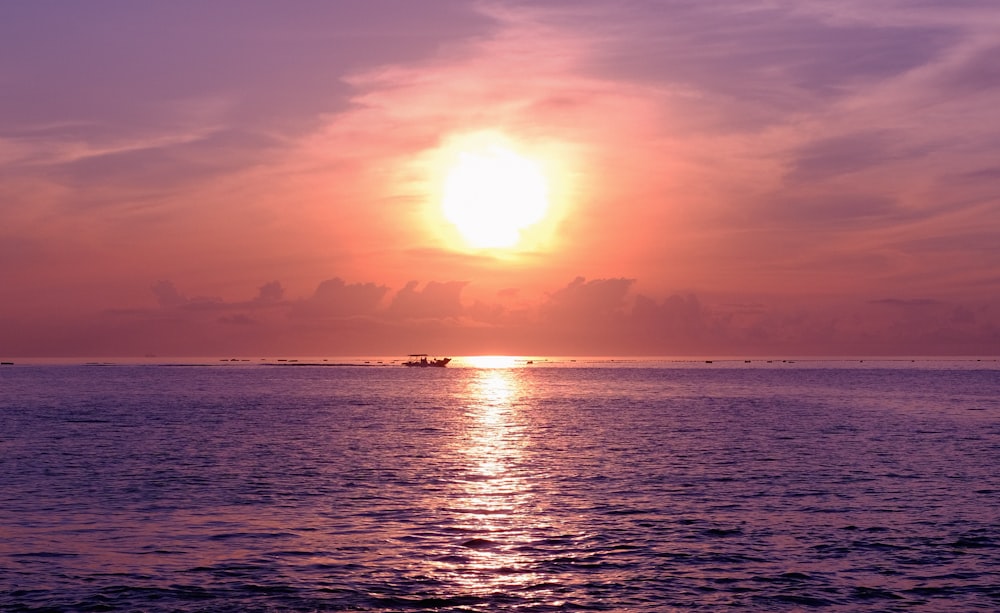 the sun is setting over the ocean with a boat in the distance