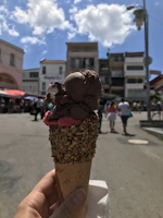 A hand holding a creamy chocolate geladinho with melting drops on a sunny day.