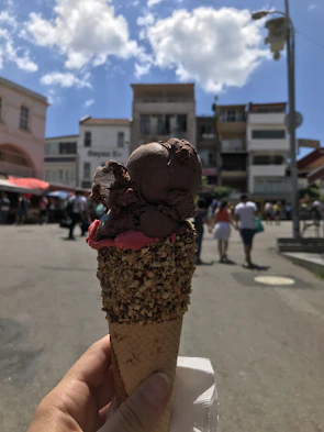 A hand holding a creamy chocolate geladinho with melting drops on a sunny day.