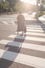 A person happily carrying grocery bags in a sunny neighborhood.