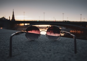 A sunny outdoor scene featuring someone wearing round tinted sunglasses with a city skyline behind.