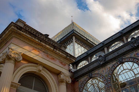 brown and black concrete building under white clouds and blue sky during daytime in El Retiro Park Spain