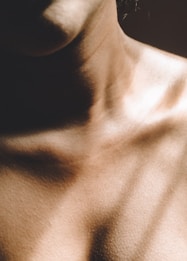 Close-up view of the human neck and shoulders with warm lighting creating soft shadows and highlights. The texture of the skin is visible, conveying a sense of realism and intimacy.