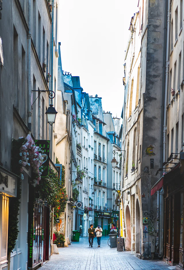 A narrow cobblestone alley lined with old buildings and shopfronts typical of Le Marais