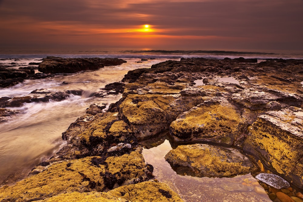 brown and gray rock formation near body of water during sunset