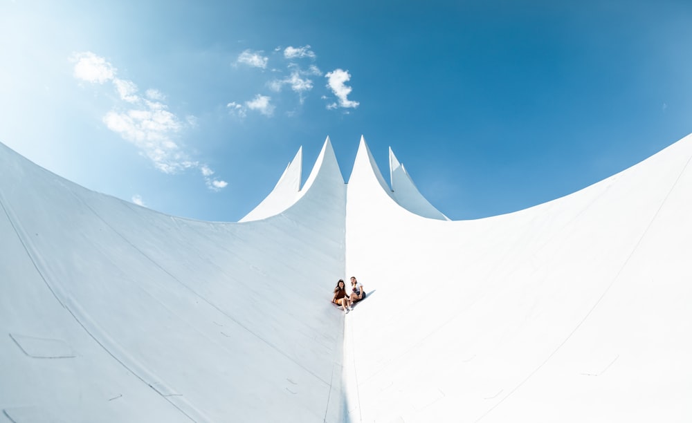 Persona in camicia bianca e pantaloni neri in piedi sulla neve bianca sotto il cielo blu durante il giorno