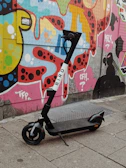 Electric scooter parked beside a graffiti-covered wall in a lively neighborhood.