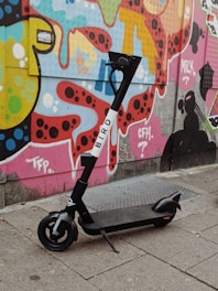 A sleek kukirin electric scooter parked on a city street with vibrant graffiti walls in the background.