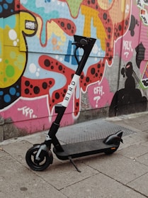 A sleek kukirin electric scooter parked on a city street with vibrant graffiti walls in the background.