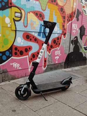 Electric scooter parked beside a graffiti-covered wall in a lively neighborhood.
