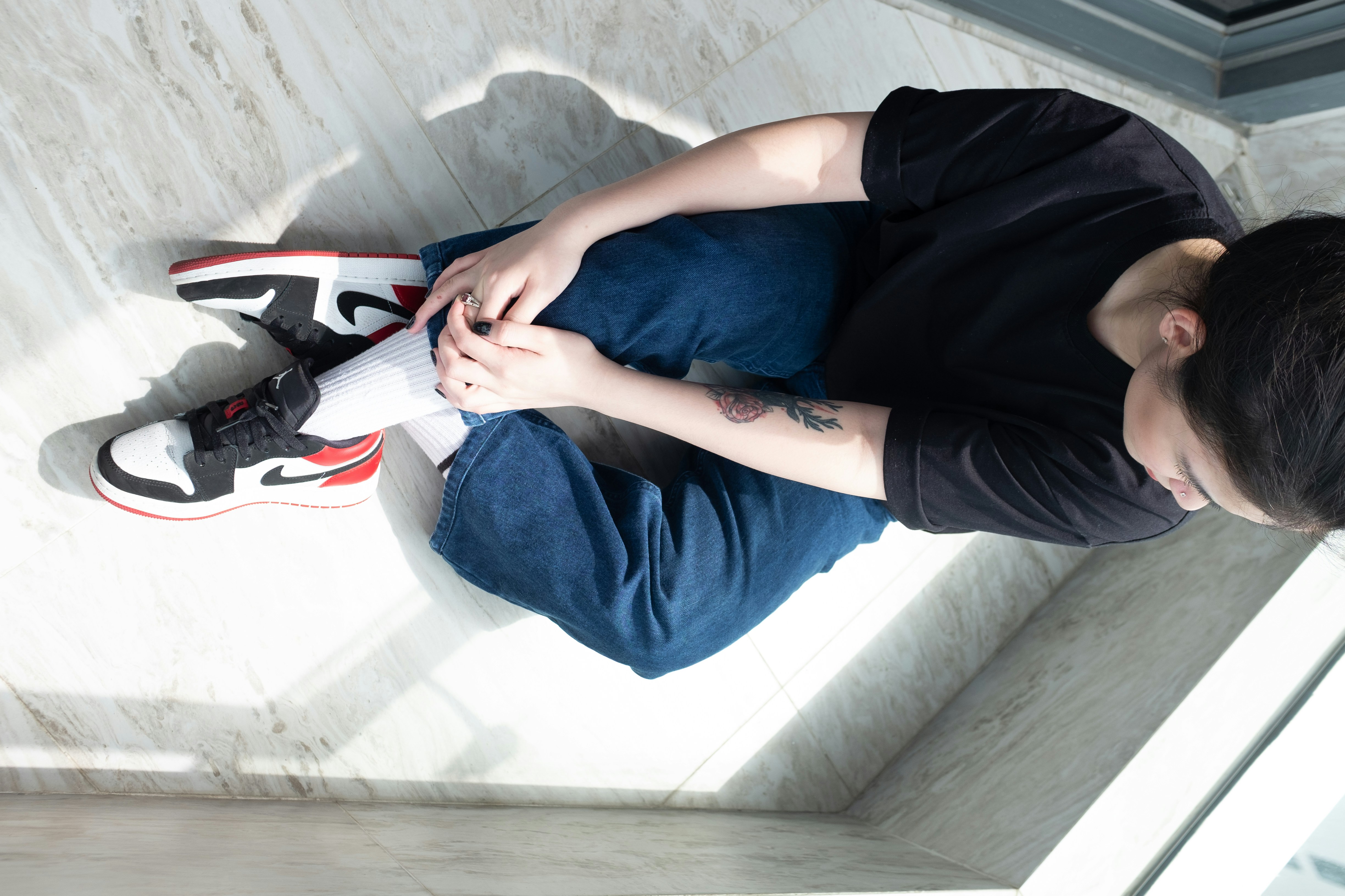 person in black t-shirt and blue denim jeans sitting on white floor