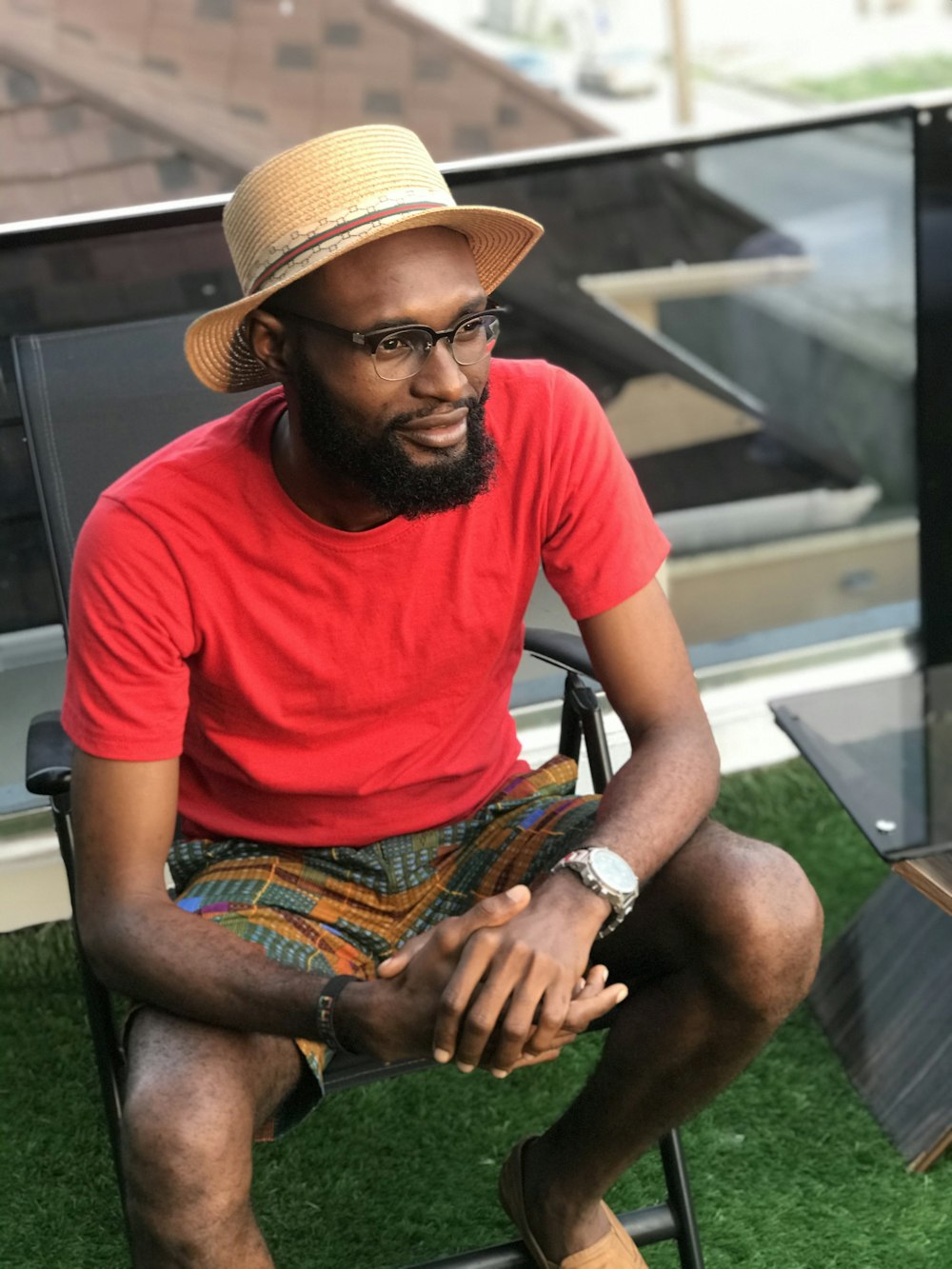 man in red crew neck t-shirt and brown hat sitting on green grass during daytime