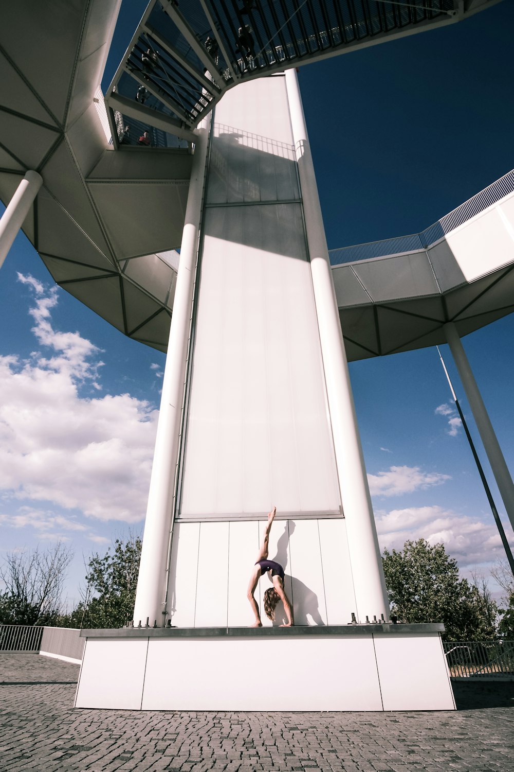 Femme en chemise blanche et jean bleu debout près d’un bâtiment en béton blanc pendant la journée