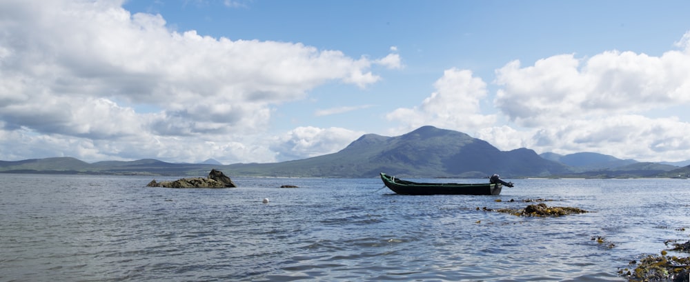 black boat on sea near mountain under blue sky during daytime