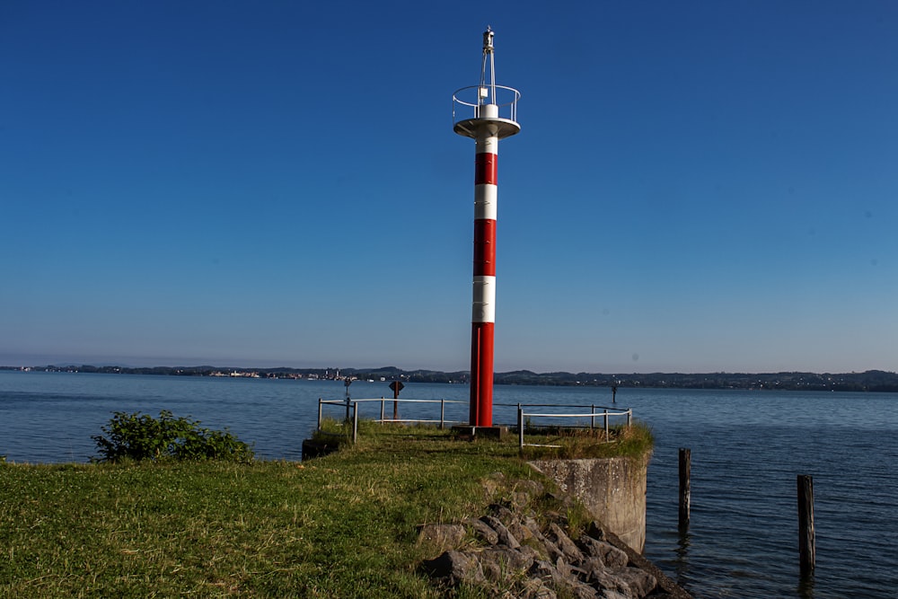 Weißer und roter Leuchtturm in der Nähe des Gewässers tagsüber
