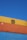 Several stacked shipping containers with distinct colors, including yellow, orange, and blue, are visible against a clear blue sky. Industrial branding and logos are imprinted on the containers.