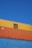 Several stacked shipping containers with distinct colors, including yellow, orange, and blue, are visible against a clear blue sky. Industrial branding and logos are imprinted on the containers.