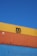 Several stacked shipping containers with distinct colors, including yellow, orange, and blue, are visible against a clear blue sky. Industrial branding and logos are imprinted on the containers.