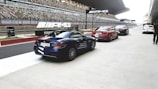 A row of luxury cars is parked alongside a modern racing track, with AMG branding visible on banners overhead. The setting appears to be a high-performance driving event, with the pit lane area and grandstands in the background.