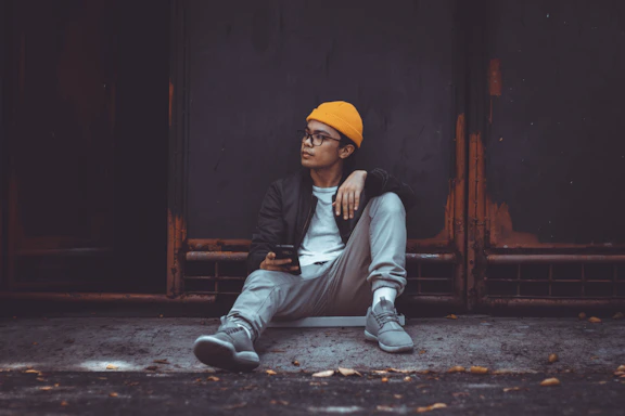 Close-up of a streetwear man typing on his phone against a moody black and orange background.