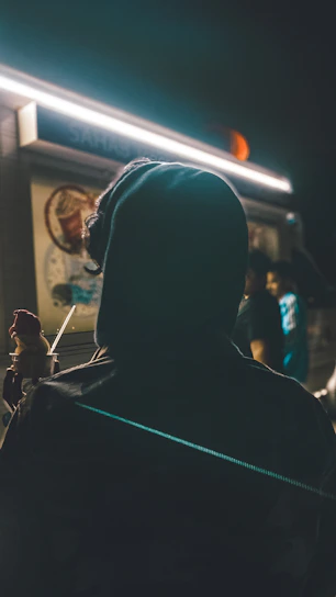 Volunteers in black hoodies and masks handing out meals under dramatic streetlights with subtle smoke and urban textures.