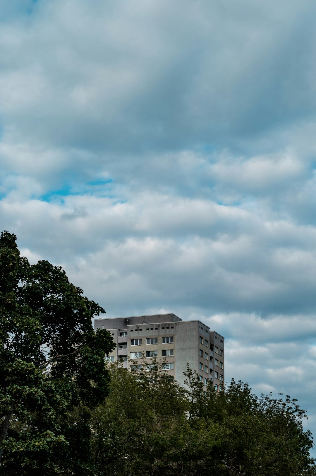 green trees near white concrete building under white clouds during daytime