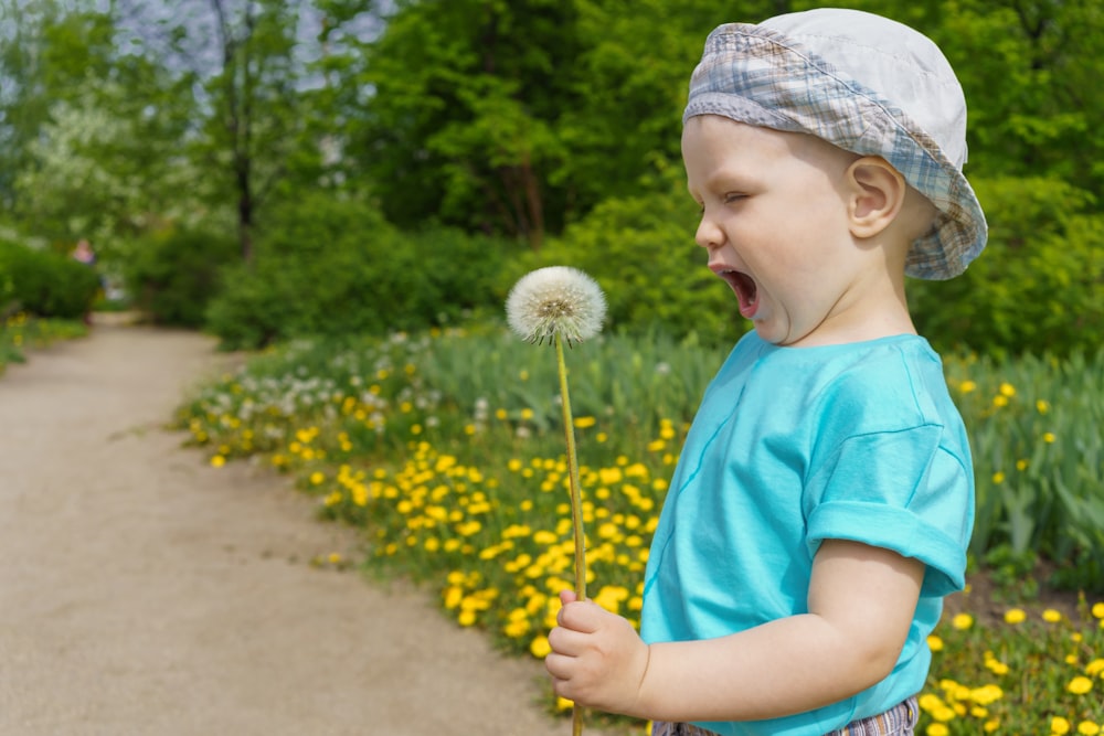 girl in blue shirt holding white dandelion flower during daytime