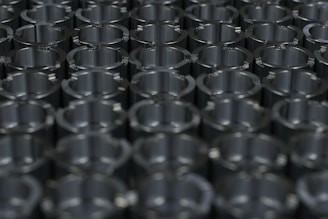 A close-up view of a grid of metallic cylindrical objects displaying a pattern of reflections and shadows on their shiny surfaces. The arrangement suggests precision and uniformity.