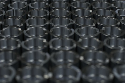 A close-up view of a grid of metallic cylindrical objects displaying a pattern of reflections and shadows on their shiny surfaces. The arrangement suggests precision and uniformity.