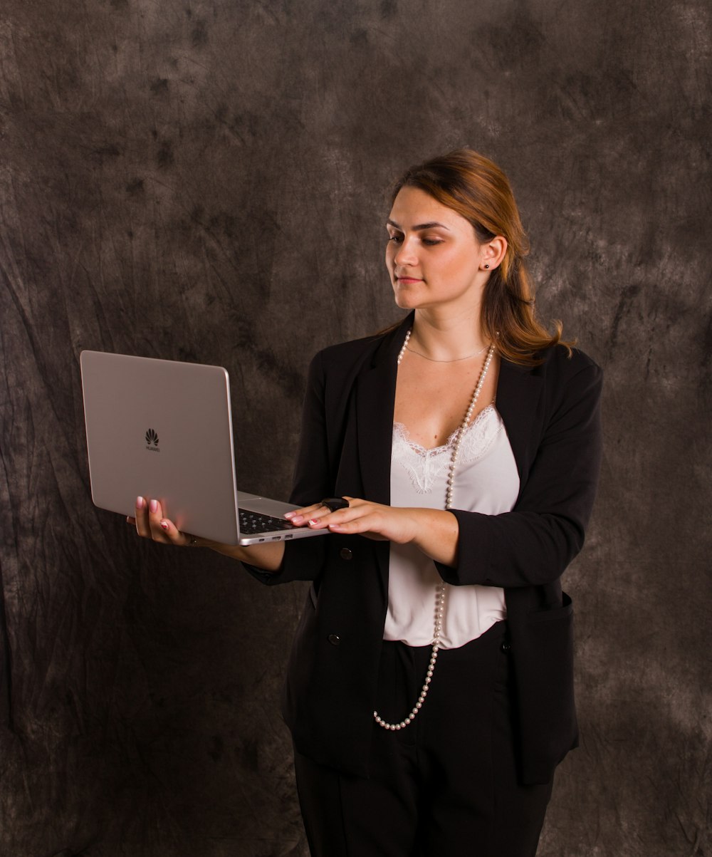 シルバーのMacBookを使用する黒いブレザーの女性