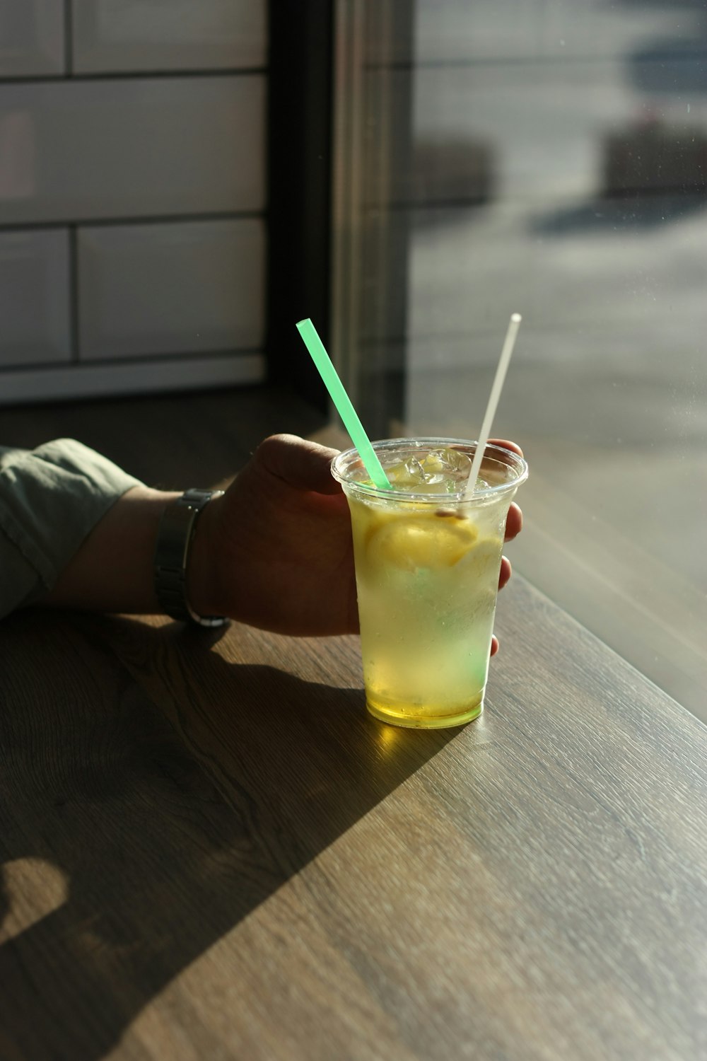 pessoa segurando copo transparente com líquido amarelo