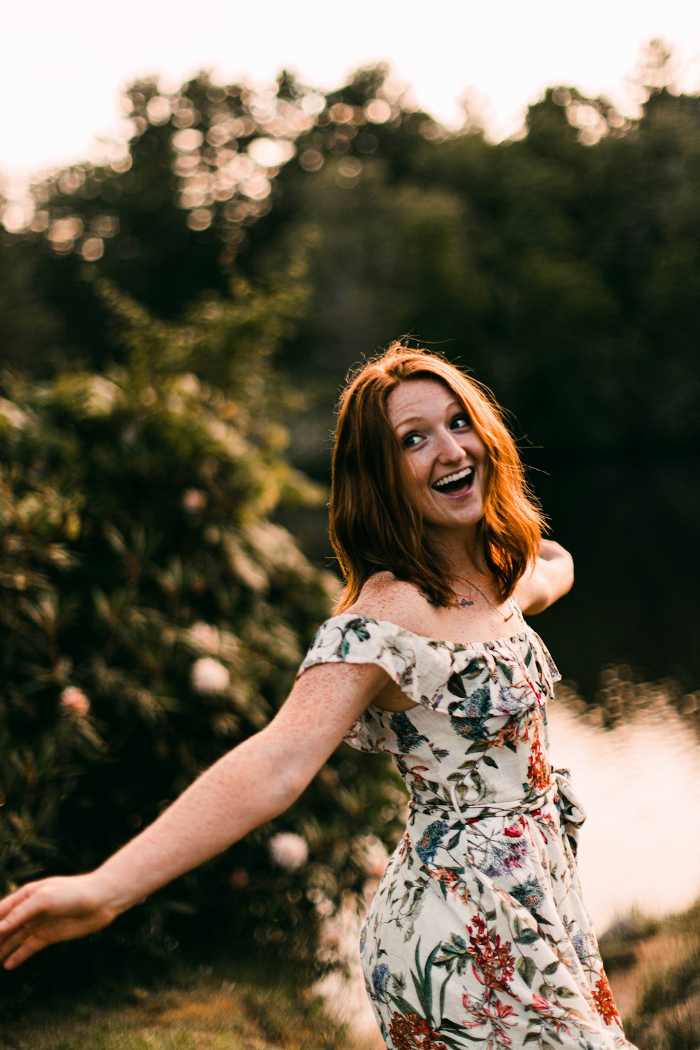 woman in white black and red floral dress standing near body of water during daytime