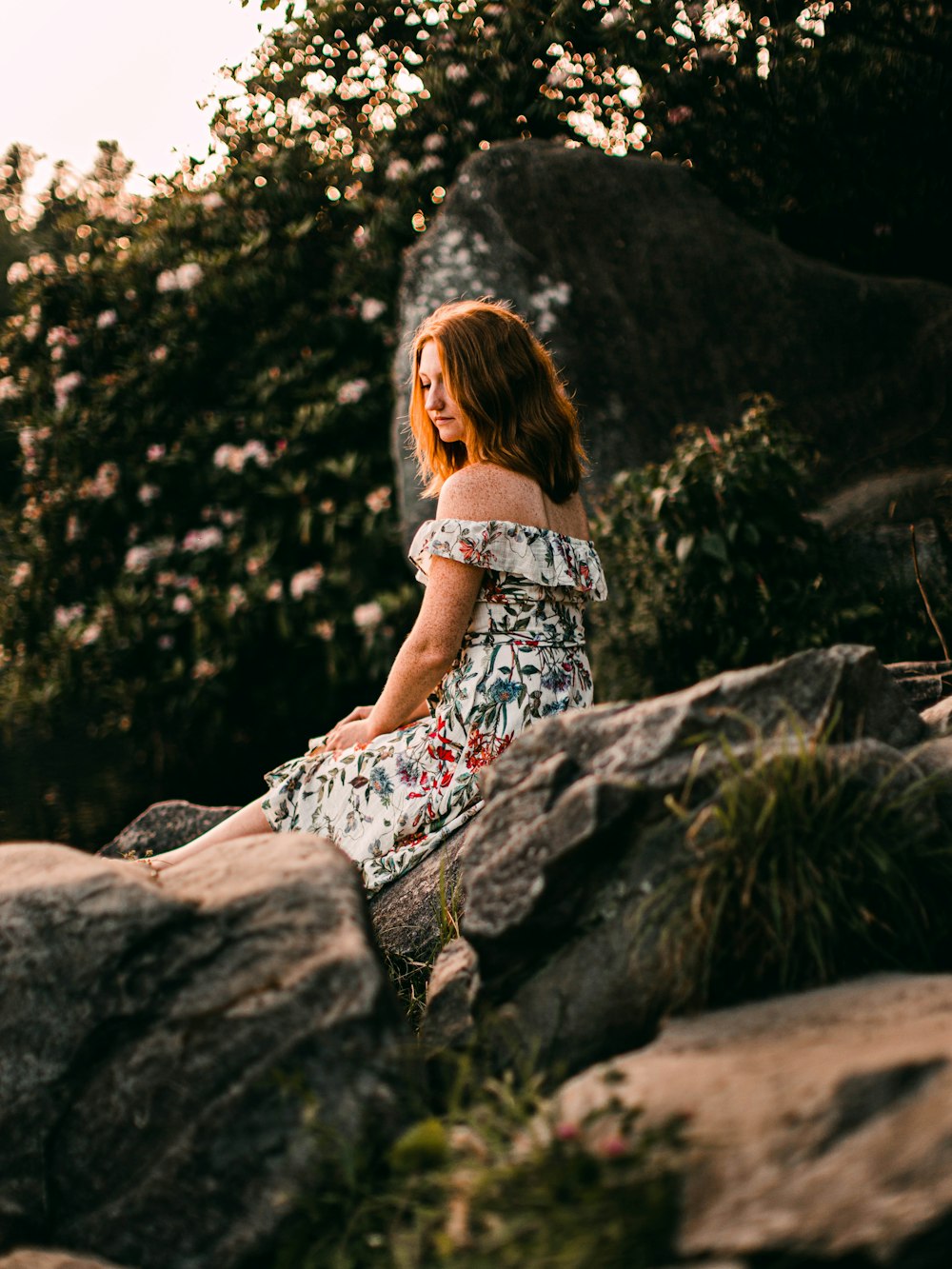 woman in white and blue floral dress sitting on rock during daytime