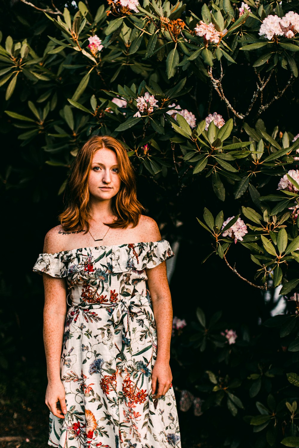 woman in white and black floral off shoulder dress standing beside green leaves